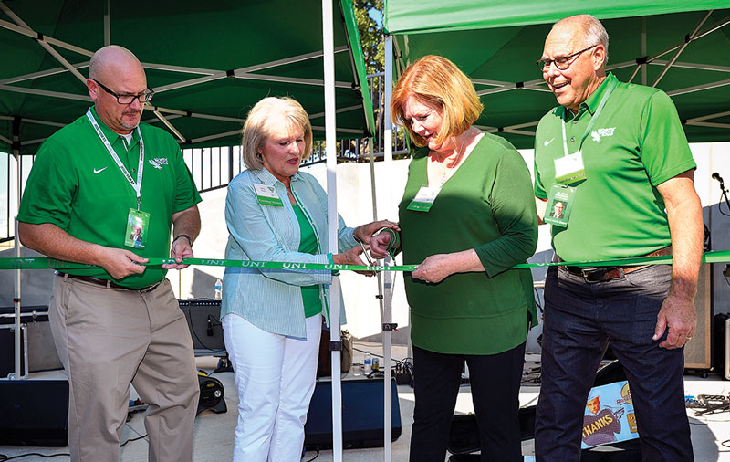 Four people in green cutting a ribbon on a patio.